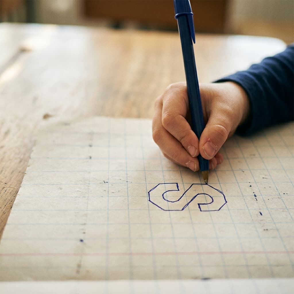 A child drawing the classic Cool S on a notebook